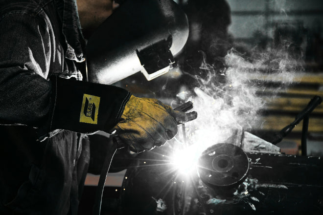 Welder using stick welding with protective gloves, helmet, and gear, highlighting safety essentials in action.