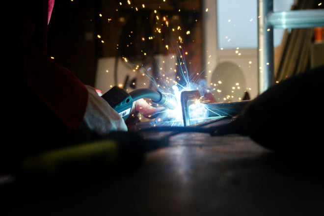 Welder using a torch to fuse metal, sparks flying in a workshop, showcasing precision welding and craftsmanship.