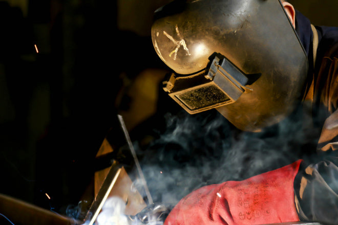 Close-up of welder working on a metal joint using arc welding, showing protective gear and joint preparation in progress.